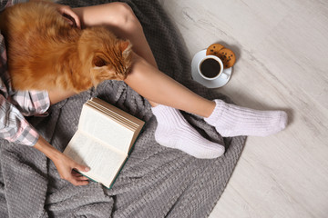 Woman with cute red cat and book on floor, top view