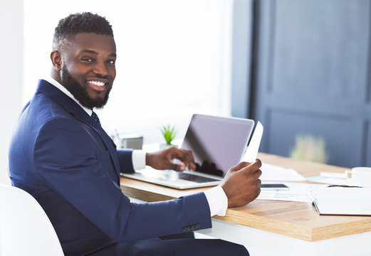 Cheerful Black General Manager Checking Reports, Sitting In Office