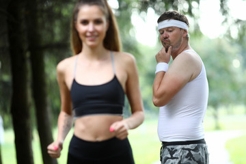 Obese man doing morning jogging in park. A girl with great figure runs by. The guy turns around look and surprisingly evaluates quality of body. Wow girls meme concept - obrazy, fototapety, plakaty