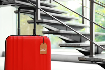 Red suitcase with TRAVEL INSURANCE label at stairs indoors, space for text