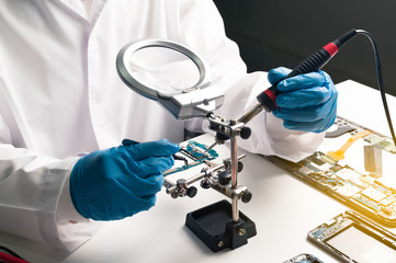 The technician is fixing the smartphone motherboard in the laboratory, with the copying area. The concept of computer hardware, mobile phones, electronics, repairs, upgrades and technology