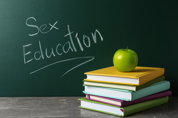 Books and apple on grey table near chalkboard with phrase 