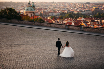 Obraz premium Newlyweds walk on wide square of cobblestones, which offers views of city