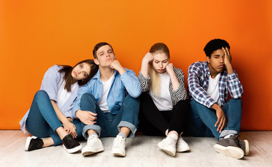 Bored classmates sitting over orange studio background