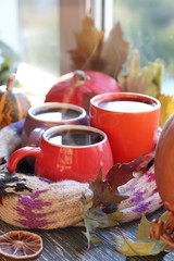 Obraz na płótnie Canvas Three cups of coffee, pumpkins, leaves, a woolen scarf on a window background, the concept of home comfort, family, Thanksgiving, autumn season