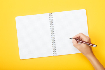 Hand with a brush over paints and blank paper on a yellow background. Mock up with copy space for your ideas. Flat lay style.