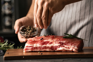 Man cooking fresh raw meat with pepper and rosemary on table, closeup - Powered by Adobe