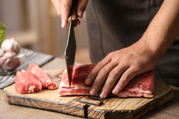 Man cutting fresh raw meat on table in kitchen, closeup