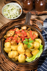 Fried pieces of chicken with red peppers and onions.