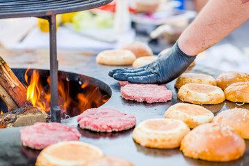 cook hands in gloves grill burger beef patties on the grill. Open fire on the barbecue