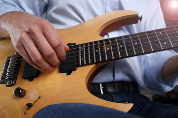 Fototapeta premium Male arms holding and playing classic shape wooden electric guitar closeup. Six stringed learning musical school education art leisure electrical vintage stage shop having fun enjoying hobby concept