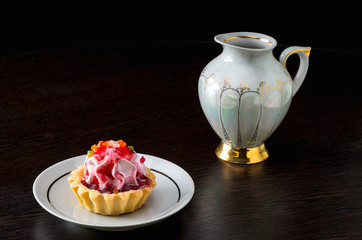 Basket-cake with jam and milk jug on dark background