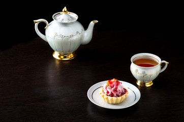 Basket-cake with jam, tea cup and tea kettle on dark background.