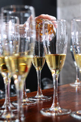A large number of glasses with white wine at the bar. Wine is pouring into a glass. Wine tasting concept in a restaurant. Out of focus. Photo in the interior.