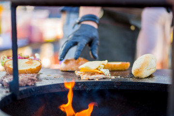 gloved hand collects a patty, cheese and vegetables on a burger roll. Ready order