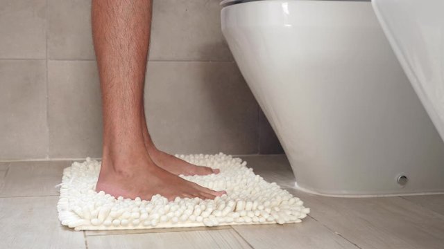 Man sitting on wc toilet bowl at the bathroom and holding a toilet paper roll, no face