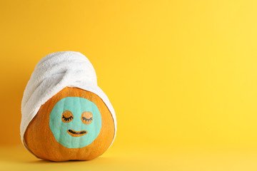 Pumpkin with facial mask and towel on yellow background, copy space