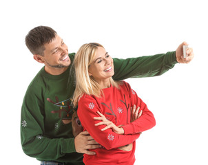 Happy couple in Christmas sweaters taking selfie on white background