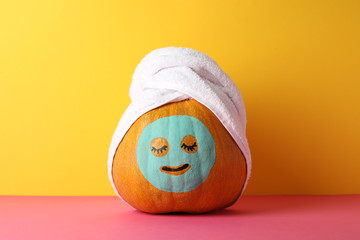 Pumpkin with facial mask and towel against yellow background, copy space