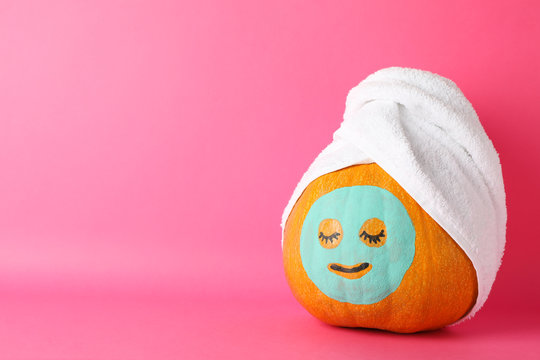 Pumpkin with facial mask and towel on pink background, copy space