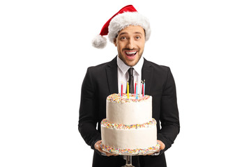 Excited young man in a suit wearing a Christmas hat and holding a cake