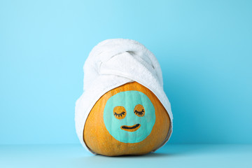 Pumpkin with facial mask and towel on blue background, copy space