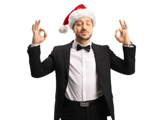 Man in a suit and bow tie wearing a Santa Claus hat and meditating