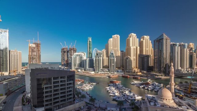 Yachts in Dubai Marina flanked by the Al Rahim Mosque and residential towers and skyscrapers aerial timelapse during all day with shadows moving fast. Modern high rise skyline with boats and wooden