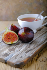 Fresh ripe figs and a white cup of tea on a wooden table.