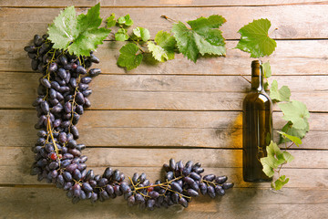 Frame made of sweet grapes and bottle of wine on wooden background