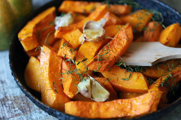 Pumpkin slices with thyme and garlic in a pan. Healthy autumn food. Vegan lunch.