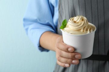 Woman holding cup with tasty frozen yogurt on blue background, closeup