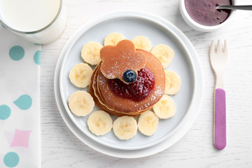 Tasty pancakes served with jam and milk on white wooden table, flat lay. Creative idea for kids breakfast