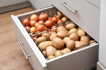 Open drawer with potatoes and onions in kitchen. Orderly storage