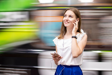 girl stands on a subway platform and listens to music on the background of a passing train, a student uses a phone in the subway, copy space