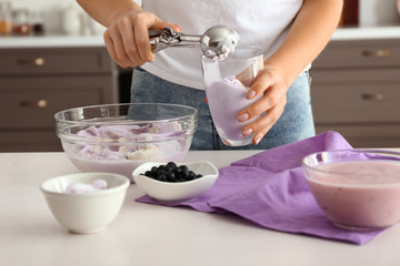 Woman putting tasty blueberry ice cream into glass in kitchen
