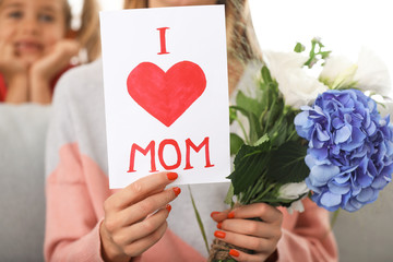 Beautiful young woman with greeting card and flowers from her daughter at home