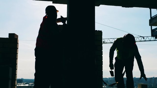 Men lay bricks, making a wall in a building.