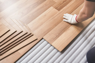 Installing laminated floor, detail on man hand in white glove fitting wooden tile, over white foam...