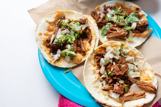 Mexican birria tacos with onion and cilantro on white background