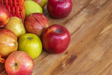 Red, green and yellow apples rolled out of a red wicker basket onto a brown wooden surface, side view from above