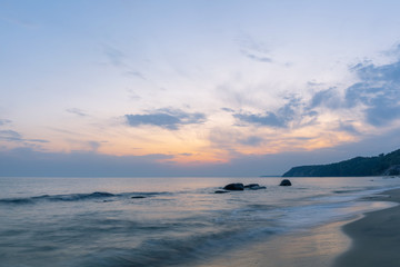 Obraz premium beautiful landscape of a wild sandy beach, a sea with protruding boulders on a long exposure and a steep coast on the horizon during sunrise