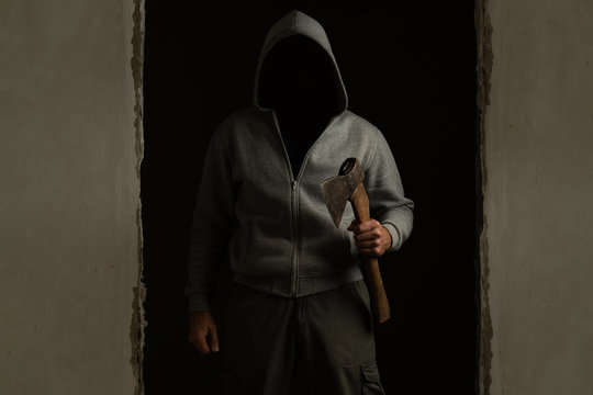 Unknown man with a hood on his head with an ax in his hand out of the dark room