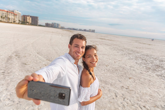 Selfie vacation beach couple romantic honeymoon. Happy young woman and man taking photo with phone - newlyweds on holdiay.