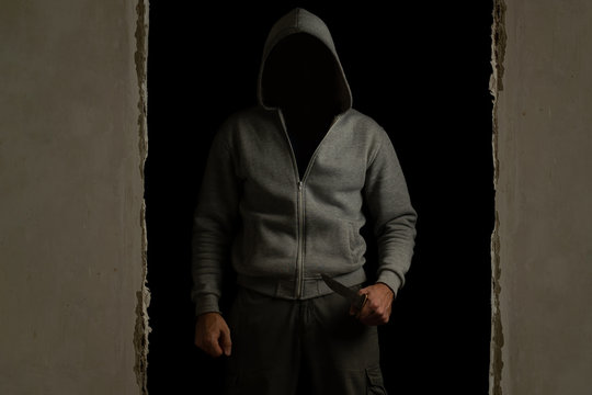 Unknown man with a hood on his head and a knife in his hand out of the dark room