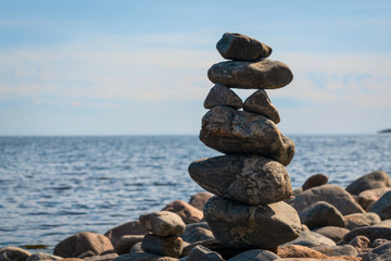 A vertical figure made of stones stands against the backdrop of water.