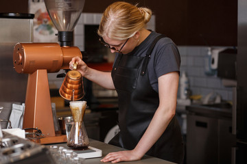 Professional barista preparing coffee using chemex pour over coffee maker and drip kettle. Young woman making coffee. Alternative ways of brewing coffee. Coffee shop concept.