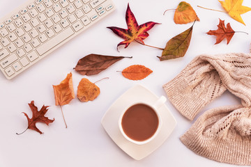 Autumn layout, coffee in white cup, yellow leaves, computer and knitted sweater. Cozy workplace, top view, copy space.