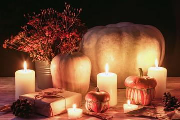 Autumn layout with pumpkins, burning candles and orange flowers in basket. Thanksgiving concept. Black background, selective focus.