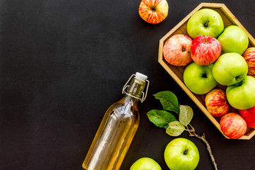 Apple cider in bottle near tray with fruits on black background top view space for text